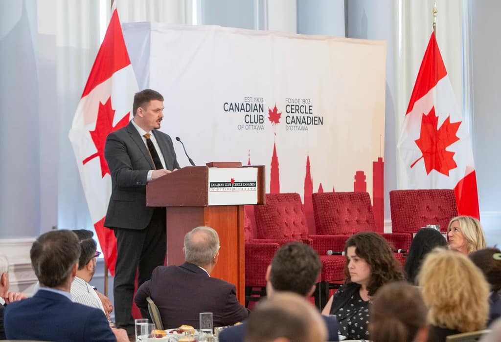 A speaker at the podium between Canadian flags