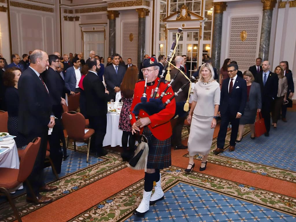 A piper in a red tunic leads a procession through a crowded banquet hall