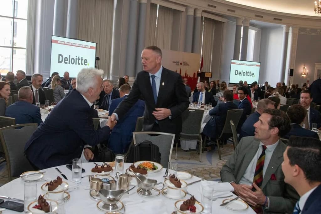 A handshake at a luncheon table, sponsor banners behind